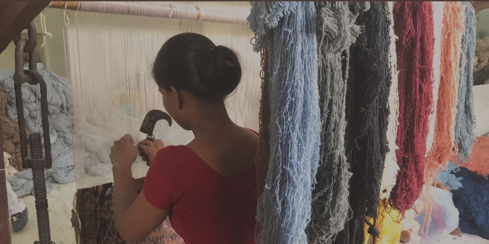 Artisan weaver making a hand-knotted wool rug on the loom with colourful skeins of wool hanging