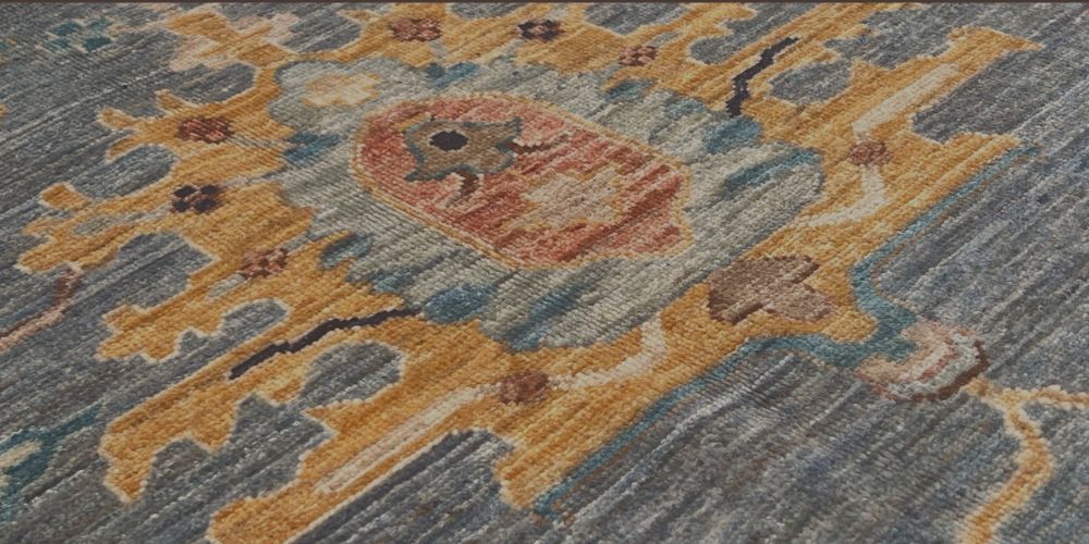 Close up of a traditional hand knotted wool rug featuring an intricate gold medallion on an indigo blue field with horizontal abrash colour variation